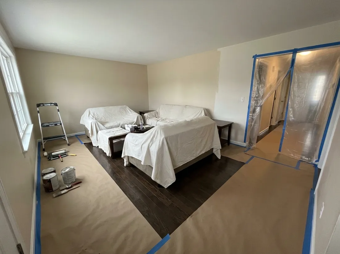 Furniture moved to the center and covered, floors protected and the doorway sealed with plastic during interior house painting