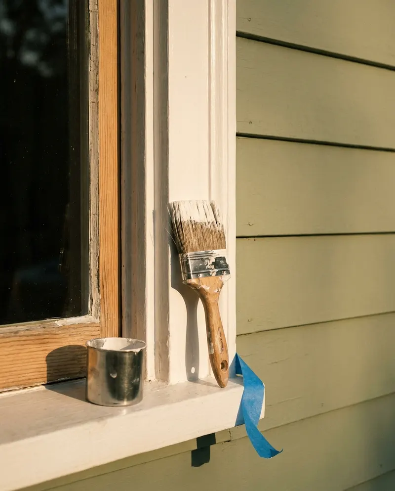 Brush and cup on the sill of a window being cut in against painted siding